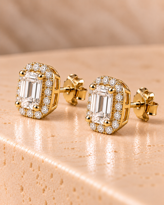 Tilt view of emerald halo diamond stud earrings in yellow gold